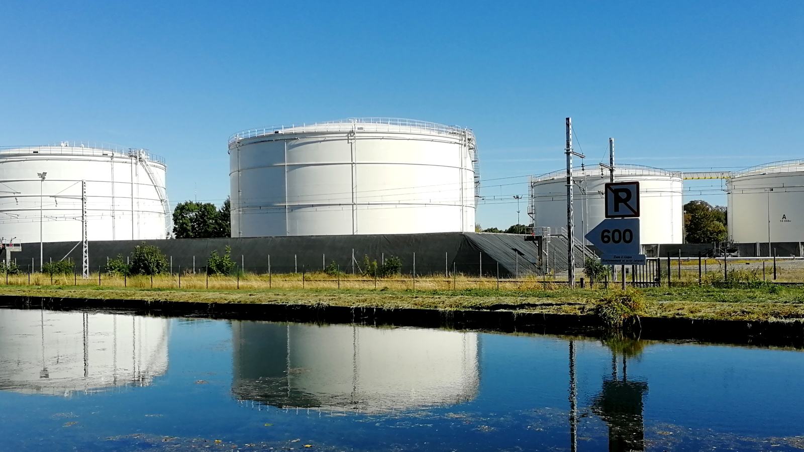 Quatre grands réservoirs blancs d'un dépôt pétrolier à Longvic, près de Dijon, qui se reflètent dans l'eau sous un ciel bleu